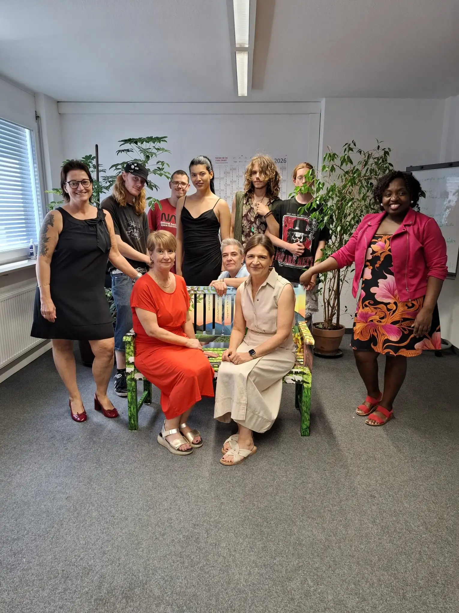 Die Teilnehmenden des MIA-Projekts übergeben gemeinsam mit Daniela Zimmermann (Leitung bfz DUA, stehend links) ihre kreativ gestaltete Motivationsbank an Christine Wible (stellvertretende Geschäftsführerin, rechts auf Bank sitzend) und Katrin Eberhardt (Teamleiterin U25). Hinter der Bank kniend Kathrin Dudziak, Coach der Maßnahme MIA, und rechts neben der Bank Charleine Yewou, Coach der Maßnahme MIA. Seite 2/1