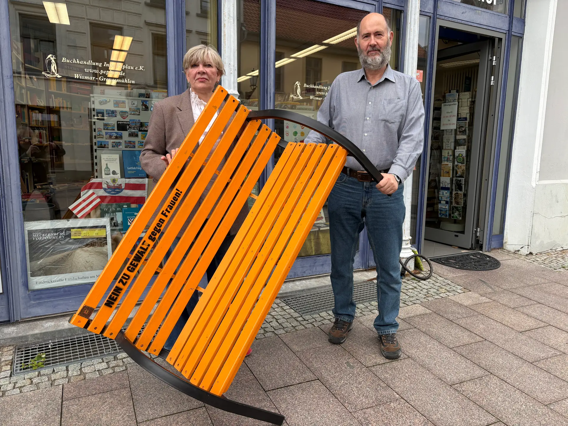 Petra Steffan, Gleichstellungsbeauftragte der Hansestadt Wismar, und Buchhändler Ralf Peplau mit der orangefarbenen Bank in der Krämerstraße in Wismar.